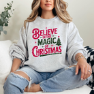 A cozy sweatshirt  with the phrase "Believe in the magic of Christmas" written in a large, all caps font. A Christmas tree and several stars surround the design.