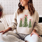 Three Christmas trees adorn this sand colored sweatshirt, each of them topped with a beautiful red bow.