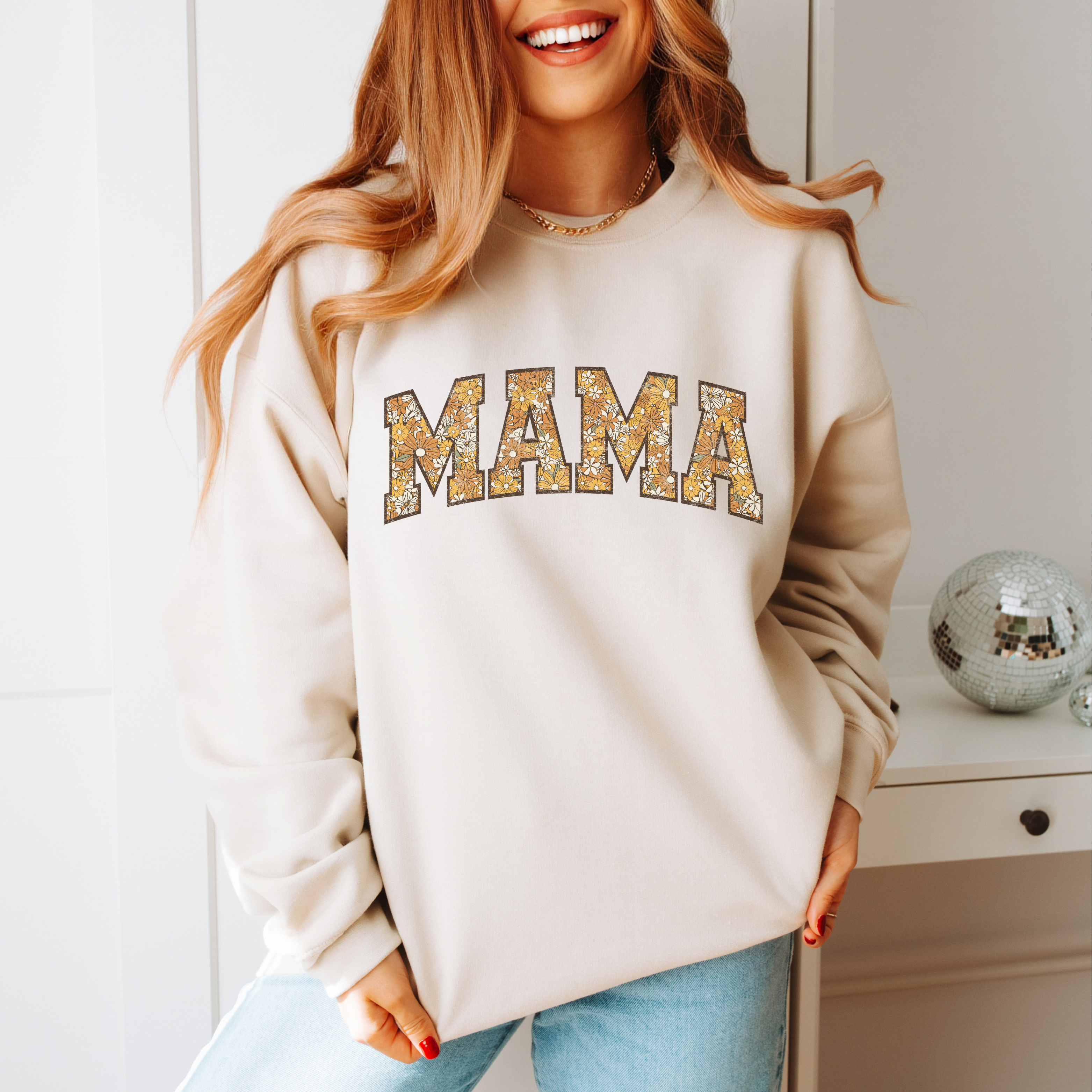 A soft, sand colored sweatshirt with the word Mama across the chest in a varsity jacket font and filled with floral patterns. 