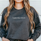 A woman wearing a dark grey sweatshirt with the words "happy days ahead," written in all lower case.